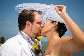 wedding portrait of bride and groom kissing at historic fort on the ocean will veil over both heads
